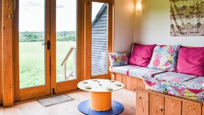 A cozy room with a wooden bench, a round table with cookies, and large windows offering a view of the outdoors. - 3 bedroom accommodation in Chelmsford (Chelmsford)