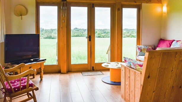 A cozy room with a wooden ceiling, a television, a chair with a polka dot cushion, a small table, and a sofa with colorful cushions. - 3 bedroom accommodation in Chelmsford (Chelmsford)