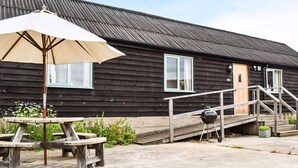 A rustic wooden building with a metal roof, a wooden staircase leading to a door, and a picnic table with an umbrella. - 3 bedroom accommodation in Chelmsford (Chelmsford)