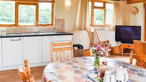 A cozy kitchen with a wooden table set for tea, a television, and a window overlooking greenery. - 3 bedroom accommodation in Chelmsford (Chelmsford)