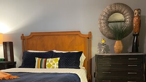 A bedroom with a wooden bed, a nightstand, a dresser, and a large mirror on the wall.