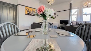 En matplats med ett runt bord, stolar, en vas med blommor och en tavla på väggen.