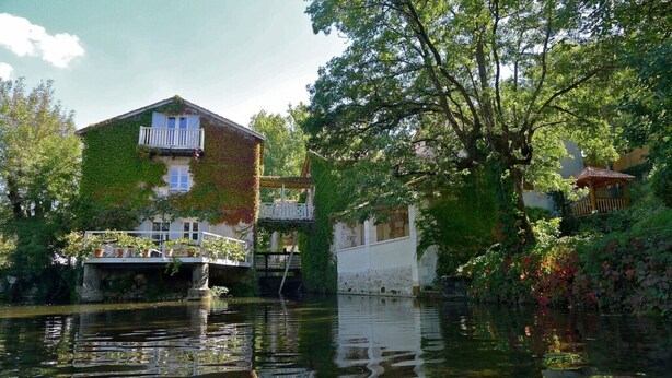 A building with a balcony and a bridge over water, surrounded by greenery.