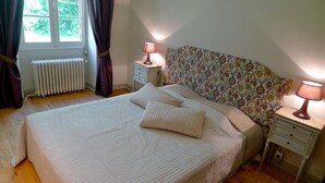 A bedroom with a large bed, two bedside tables with lamps, a radiator, and a window with curtains.