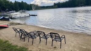 A lakeside area with a dock, boats, and a row of metal chairs on the sandy shore. - Lake House on Jose Lake (South Branch)