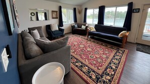 A living room with a gray sofa, a blue armchair, and a patterned rug. - Lake House on Jose Lake (South Branch)