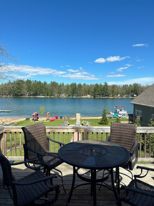 A deck with outdoor furniture overlooking a lake, boats, and a forested shoreline. - Lake House on Jose Lake (South Branch)