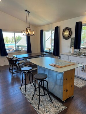 A modern kitchen with a central island, bar stools, a hanging light fixture, and a view of a backyard. - Lake House on Jose Lake (South Branch)