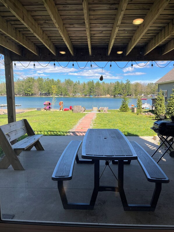 An outdoor covered picnic area with a wooden table and benches, overlooking a lake with boats and a dock. - Lake House on Jose Lake (South Branch)