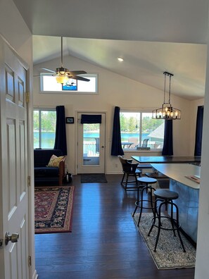 A spacious kitchen with a high ceiling, a dining area with bar stools, and a view of a lake through the windows. - Lake House on Jose Lake (South Branch)