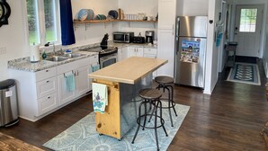 A modern kitchen with white cabinets, a stainless steel refrigerator, and a wooden island with stools. - Lake House on Jose Lake (South Branch)