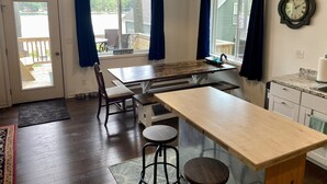 A kitchen with a wooden table, chairs, a hanging light, and a clock on the wall. - Lake House on Jose Lake (South Branch)