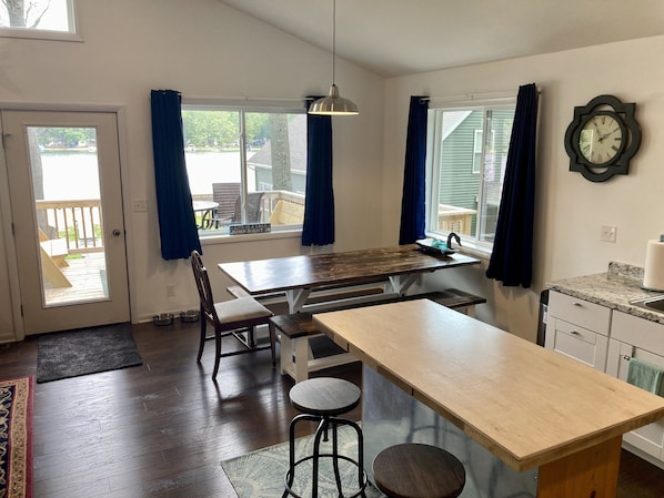 Een keuken met een houten tafel, stoelen, een hanglamp en een klok aan de muur.