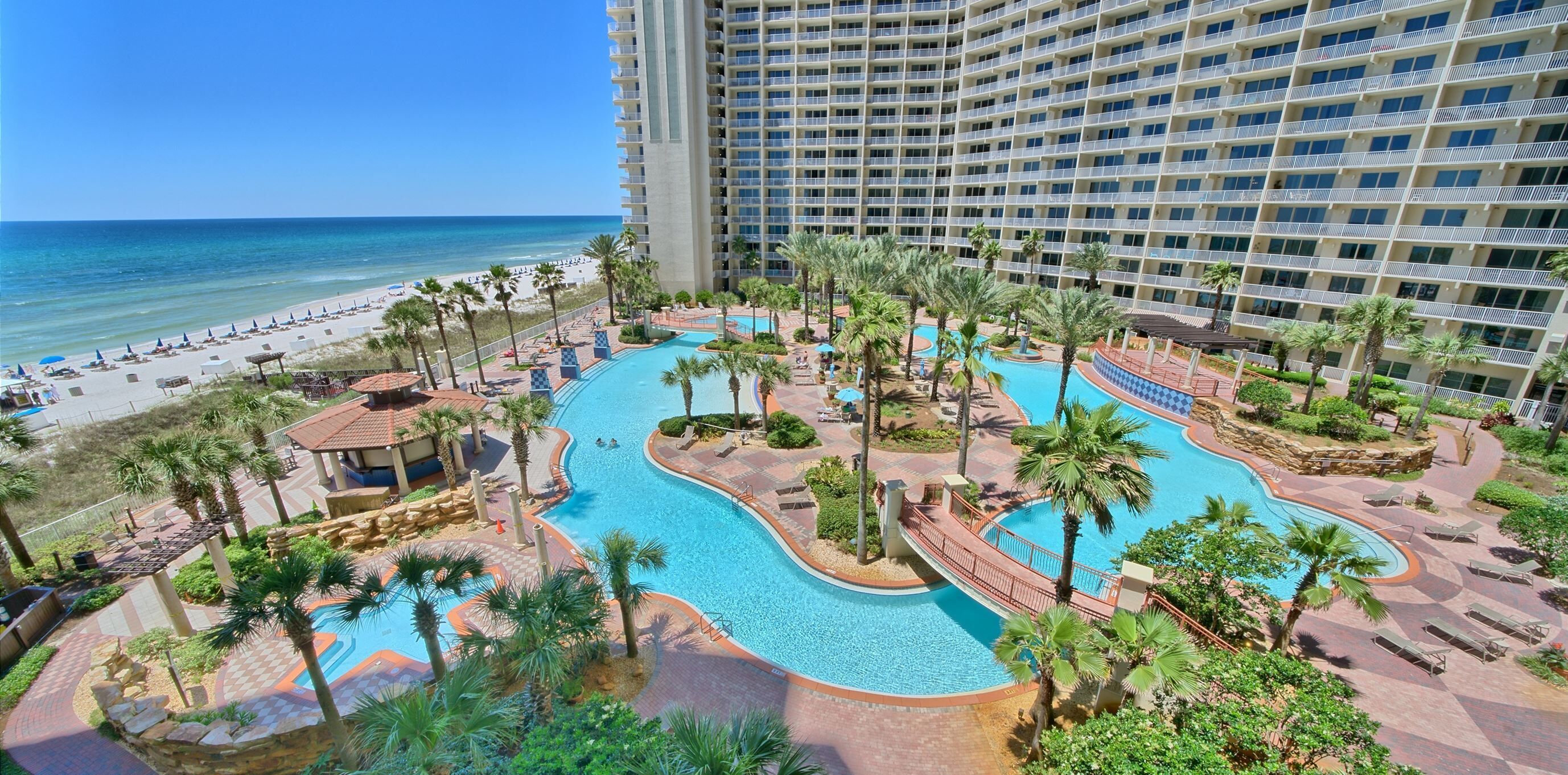 A resort with a large swimming pool, palm trees, and a beach view.