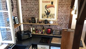 A kitchen with a brick wall, wooden cabinets, a black countertop, and a poster on the wall. - House with garden and free parking, 2 minutes from Le Clos Lucé (Amboise)
