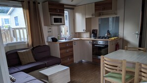 Eine kleine Küche mit Mikrowelle, Herd und Spüle. Ein Holztisch mit Stühlen und ein Sofa mit Kissen sind ebenfalls vorhanden.