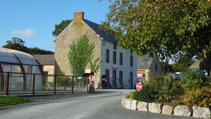 Ein Steinhaus im traditionellen Baustil, links davon eine Glashauskonstruktion und im Vordergrund ein Verbotsschild.