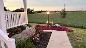 A porch with a white railing, a concrete pathway, and a garden with various flowers.
