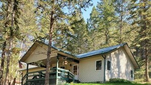A single-story house with a porch, surrounded by a well-maintained lawn and tall pine trees. - Secluded Montana home on five acres (Rexford)