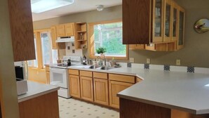 A kitchen with wooden cabinets, a white stove, and a window with a view of greenery. - Secluded Montana home on five acres (Rexford)