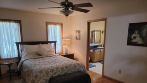 A bedroom with a bed, a nightstand, a lamp, a ceiling fan, and a view into the bathroom. - Secluded Montana home on five acres (Rexford)
