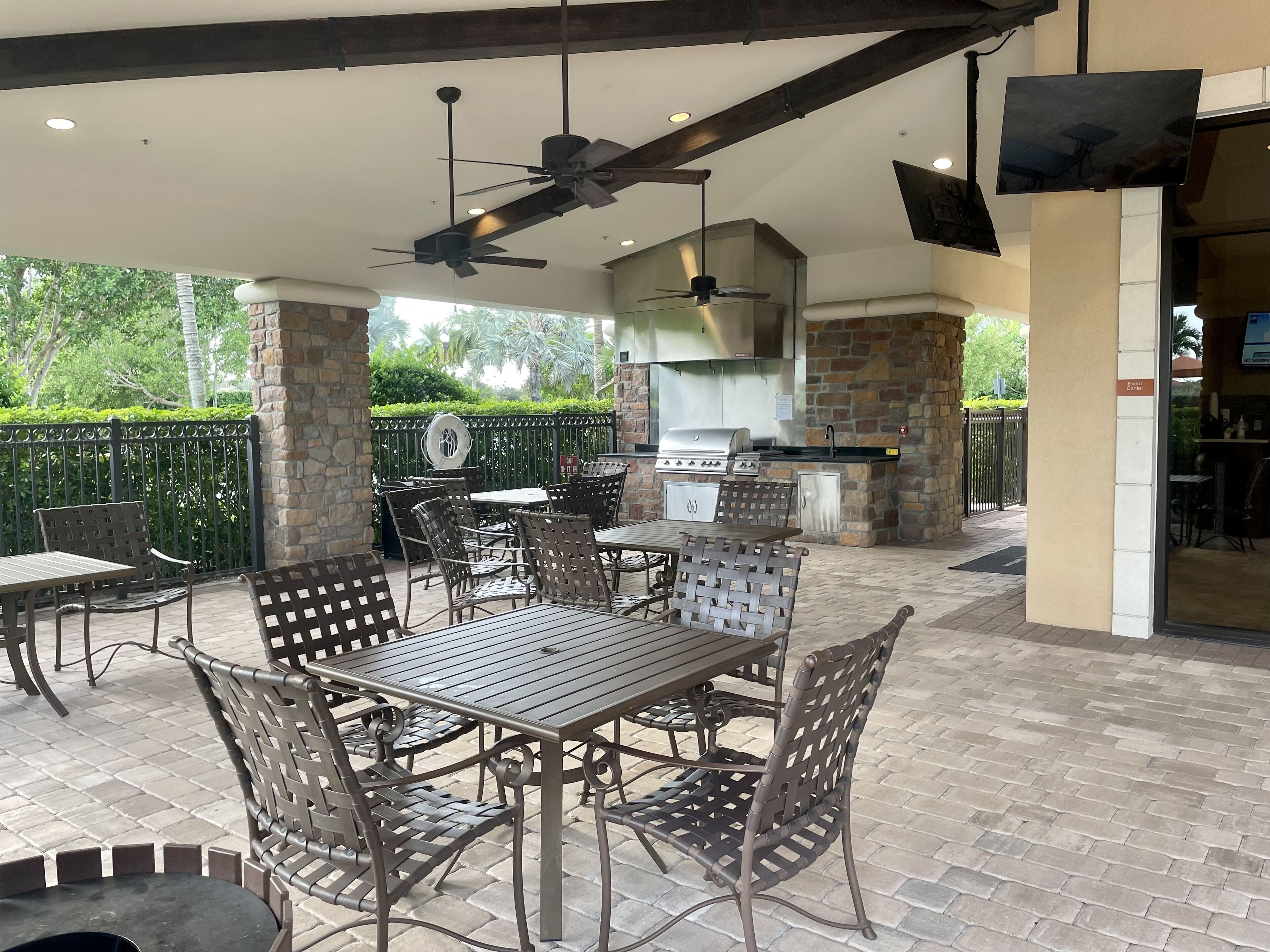An outdoor patio area with a brick floor, metal tables and chairs, a ceiling fan, and a stone barbecue grill.