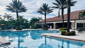 Ein Pool mit klarem Wasser, umgeben von Palmen und einem Gebäude mit einem Ziegeldach.