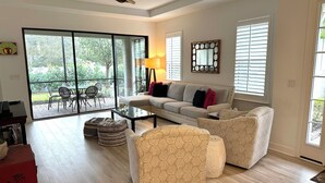 Ein geräumiges Wohnzimmer mit einer Couch, gemusterten Hocker, einem Couchtisch und einem Deckenventilator.