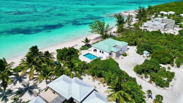 A beachfront property with a swimming pool, multiple buildings, and lush greenery.