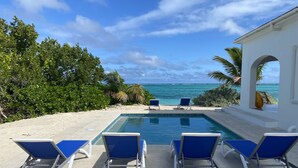 A pool area with blue lounge chairs and a view of the ocean.