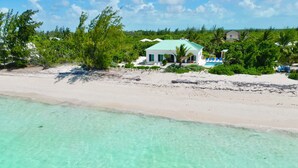 A beachfront property with a white building, clear turquoise water, and lush greenery.