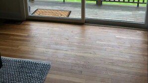 Una habitación con piso de madera, una puerta corrediza de vidrio que da a un balcón con baranda de madera y un felpudo con la inscripción "WELCOME".