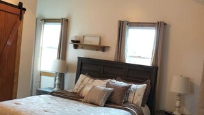 Un dormitorio con cama, mesita de noche, ventilador de techo y ventana con cortinas.
