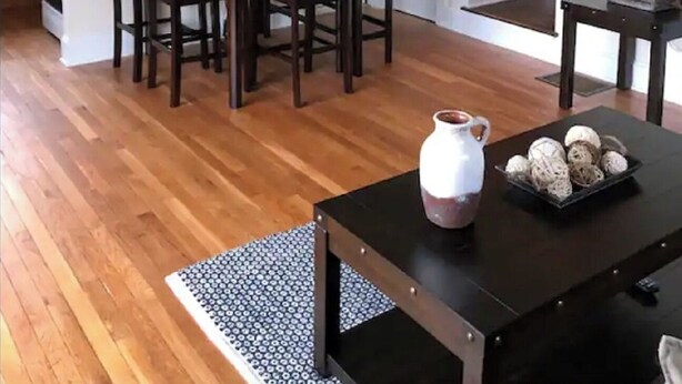 Un comedor con una mesa y sillas, un televisor montado en la pared y una escalera que sube a un nivel superior.