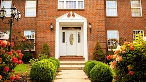 A brick building with a white front door, two windows on the upper floor, and a small porch with steps. - Holland Acres (Williamstown)