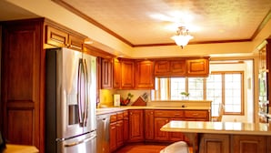 A kitchen with wooden cabinets, a stainless steel refrigerator, and a large window providing natural light. - Holland Acres (Williamstown)