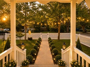 Un pasillo cubierto con valla de piquetes blancos, luces colgantes y plantas en macetas.