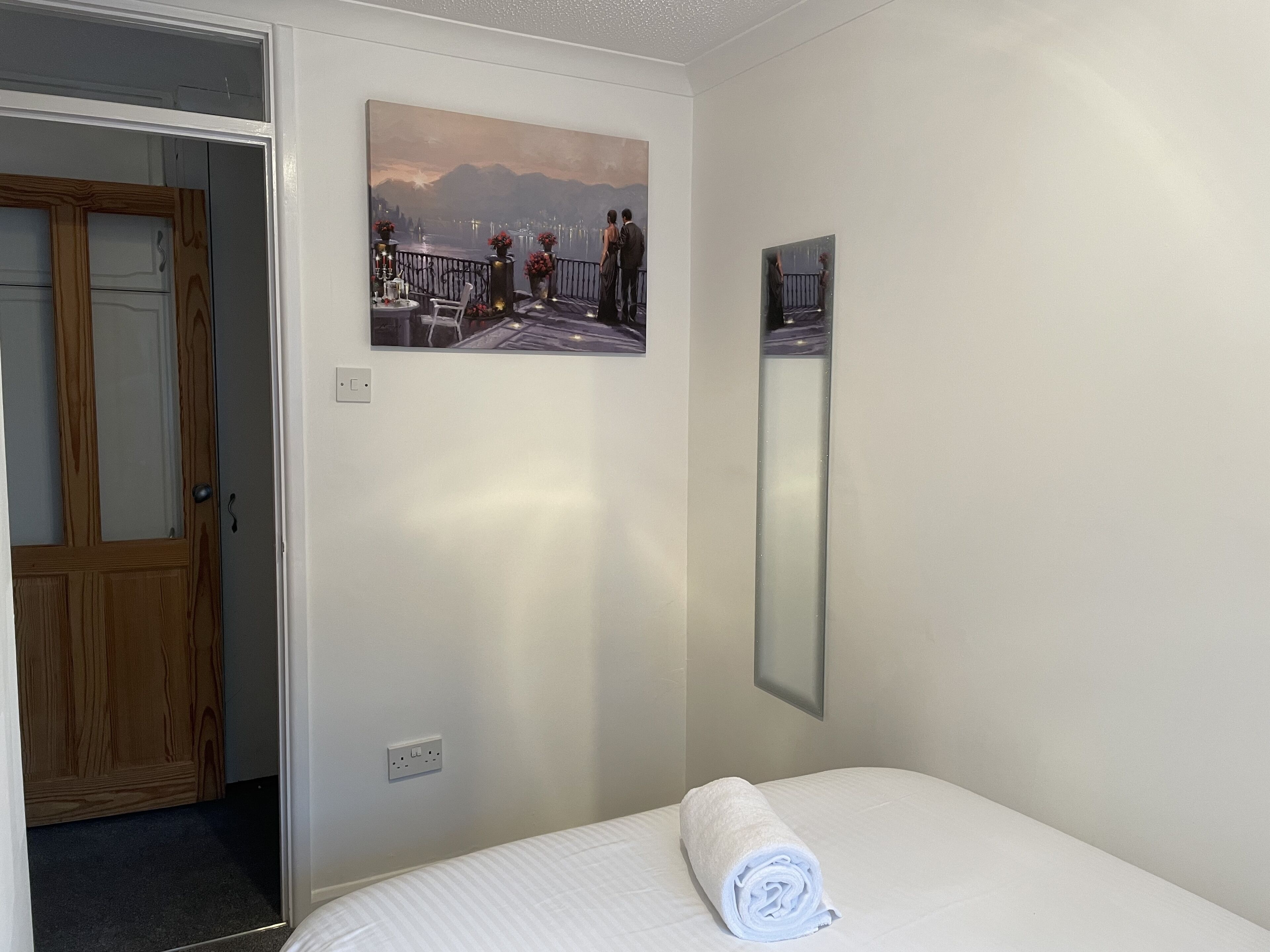Habitación de hotel con cama, un cuadro de un paisaje, un espejo y una puerta de madera.