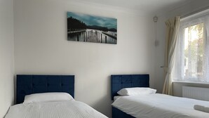A hotel room with two beds, a painting of a bridge, and a window with curtains.