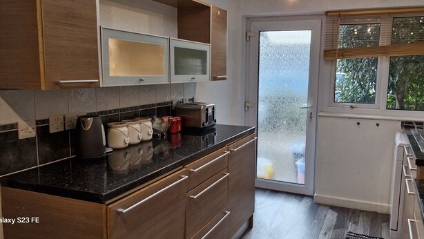 A modern kitchen with wooden cabinets, a black countertop, and a window with a view of greenery.