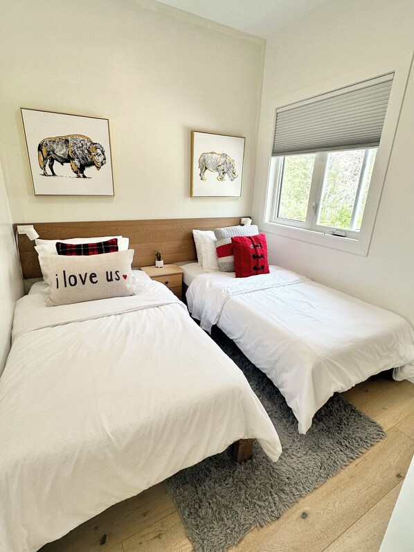 A bedroom with two beds, a window with blinds, and two framed animal illustrations on the wall.