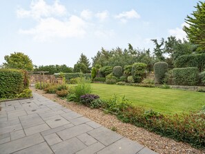 Un jardin avec un chemin de pierres menant à une pelouse, le tout entouré de différentes plantes et arbres.