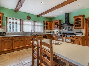 Une cuisine avec des meubles en bois, un îlot central, une cuisinière et une fenêtre avec des stores.