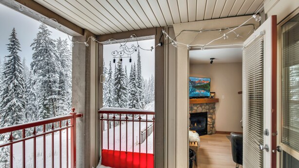 Ein Balkon mit roter Geländer, einem Steinkamin und Blick auf schneebedeckte Bäume.