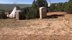 Ein Campingplatz mit einem Tipitent, mobilen Toiletten und freiem Blick auf die umliegende Landschaft.