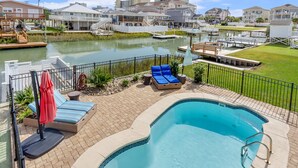 A swimming pool with lounge chairs and a red umbrella, surrounded by a brick deck and a metal fence. - Updated Family-friendly channel home with private pool & close to the beach (North Myrtle Beach)