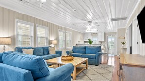 A spacious living room with a large blue sofa set, a wooden coffee table, and a kitchen area in the background. - Updated Family-friendly channel home with private pool & close to the beach (North Myrtle Beach)