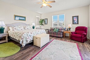 A bedroom with a bed, a red armchair, a plaid sofa, a wooden nightstand, a green rug, and a ceiling fan. - Spacious family channel home-great views, boating, fishing, kayaking-close to the beach (North Myrtle Beach)