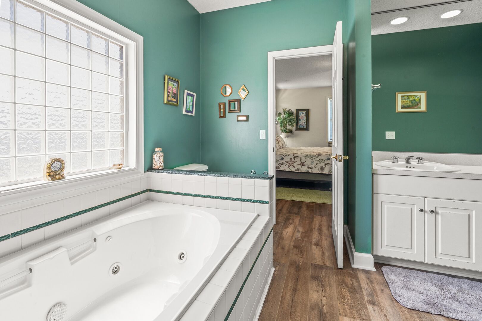 A bathroom with a large bathtub, a window, and a door leading to a bedroom.