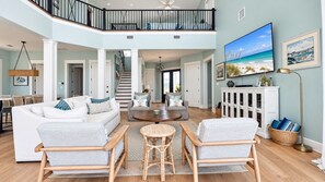 A spacious living area with a high ceiling, a staircase leading to an upper level, and a large flat-screen TV mounted on the wall.